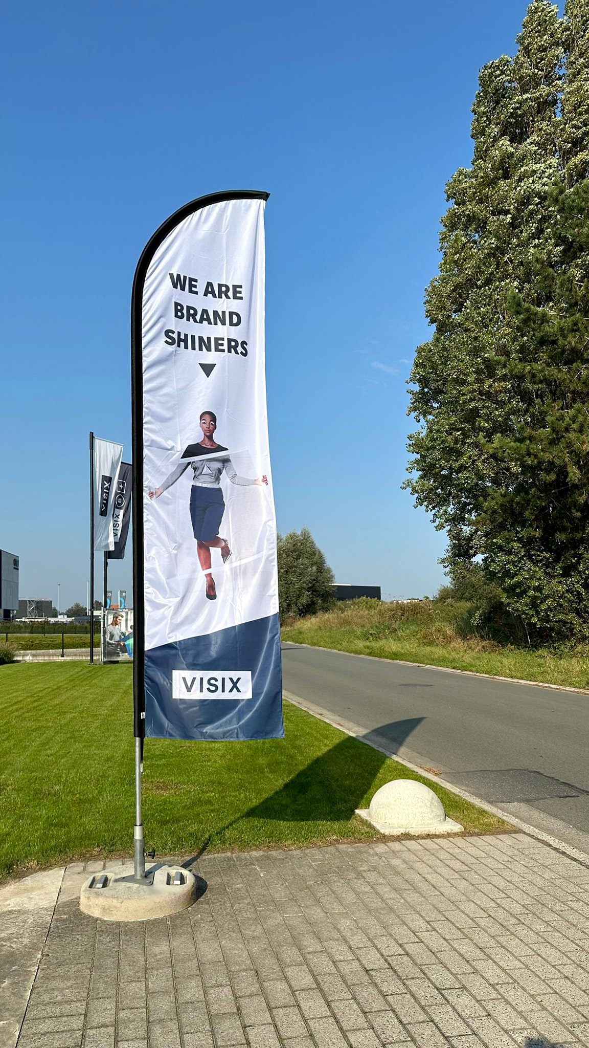 Flaga reklamowa z nadrukiem (winder) VISIX ustawiona przy drodze – mobilny nośnik reklamy outdoorowej dla firm i eventów